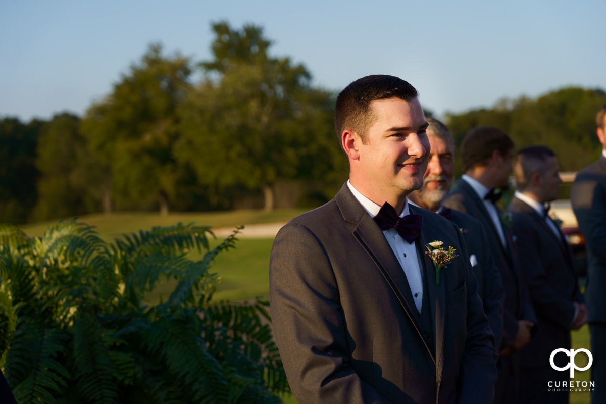 Groom smiling as his bride is walking down the aisle.