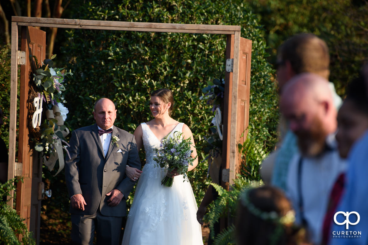 Bride and her father walking down the aisle through the wooden doors at the ceremony.