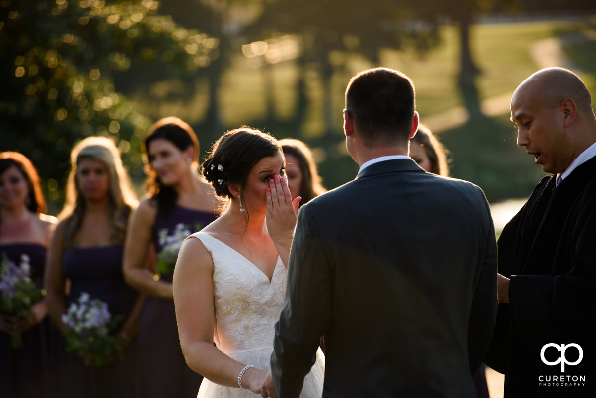Bride wiping a tear from her eye during her wedding ceremony at Holly Tree Country Club.