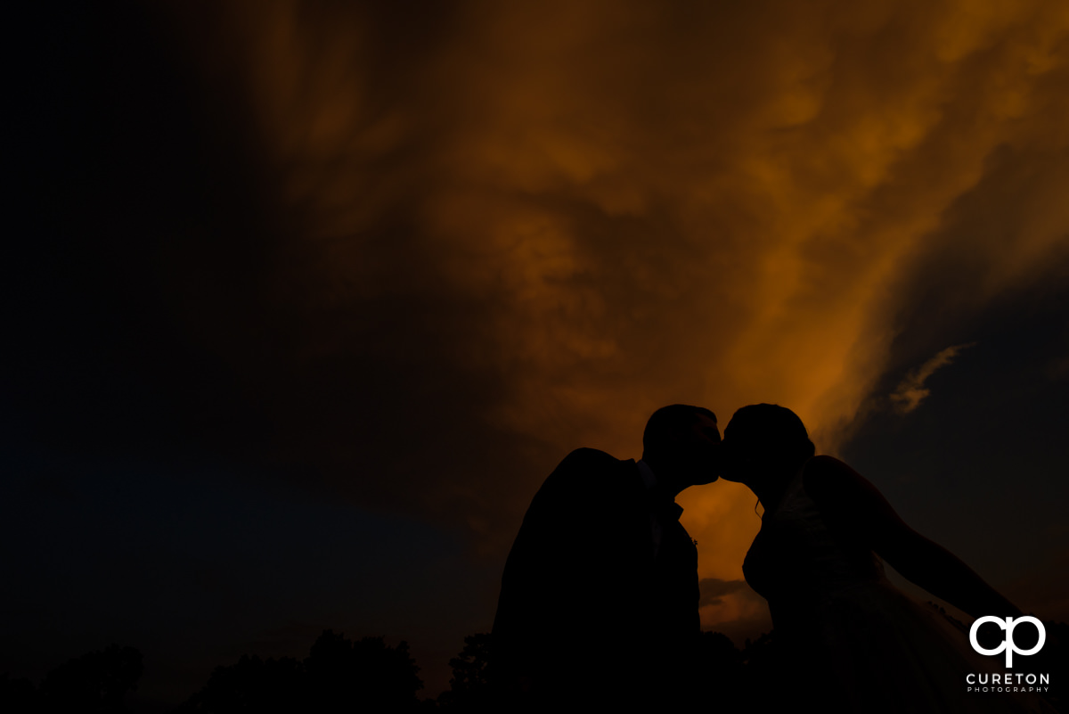 Bride and groom kissing silhouette at sunset.