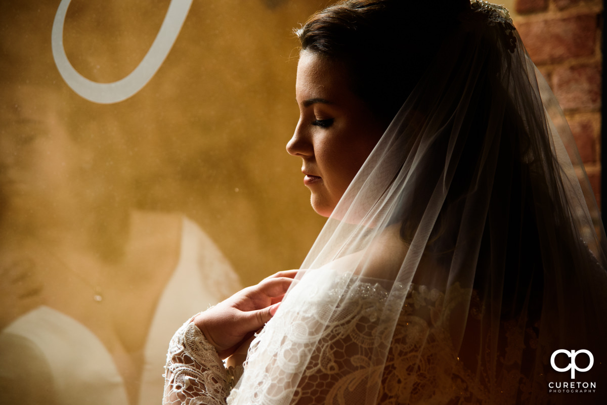 Bride looking at her veil in front of a huge bay window at The Old Cigar Warehouse in downtown Greenville,SC.