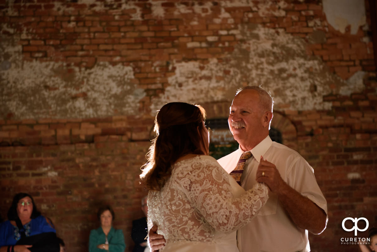 Bride's father smiling while dancing with his daughter.