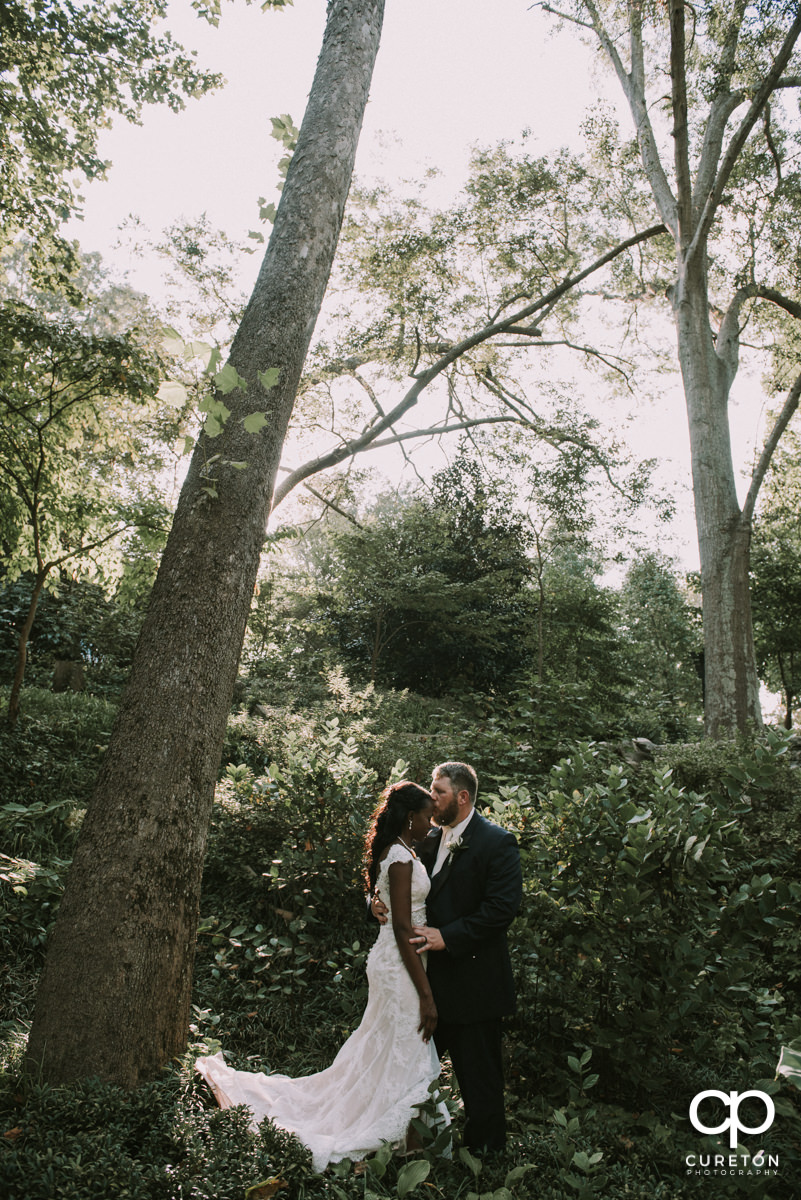 Groom kissing his bride on the forehead in the forest after their wedding ceremony at Falls Park on the Reedy in downtown Greenville,SC.