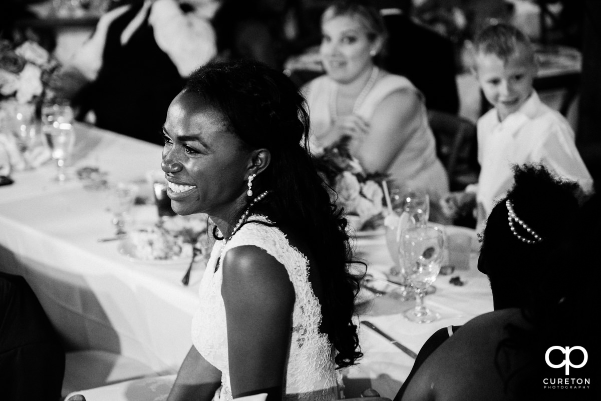 Bride smiling while her groom gives a speech.