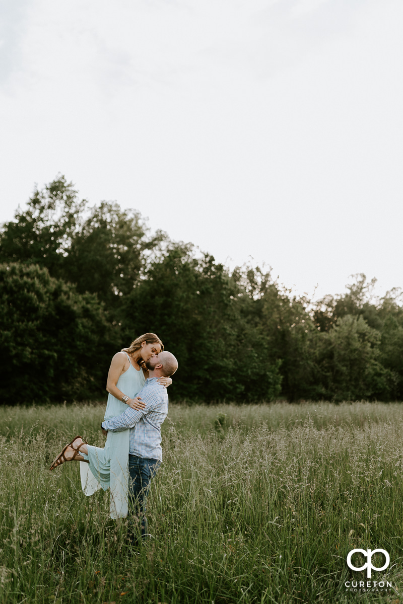 Man lifting his fiancee in a field of tall grass during a family farm engagement session in Gray Court,SC.
