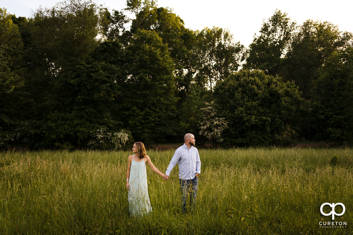 Engaged couple walking though a field of tall grass during a family farm engagement session in Gray Court,SC.