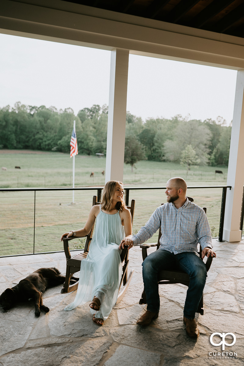 Engaged couple and their dog sitting on the front porch of a farm.