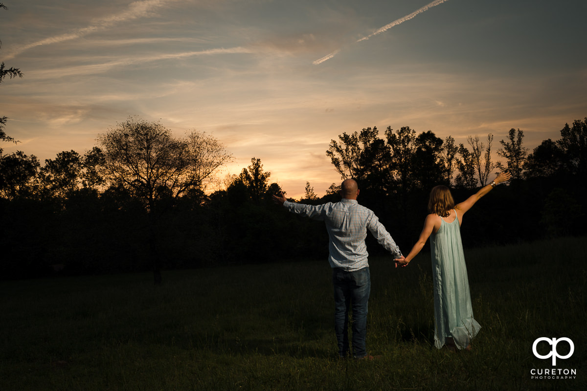 Man and woman with their hands in the air at sunset during a family farm engagement session in Gray Court,SC.