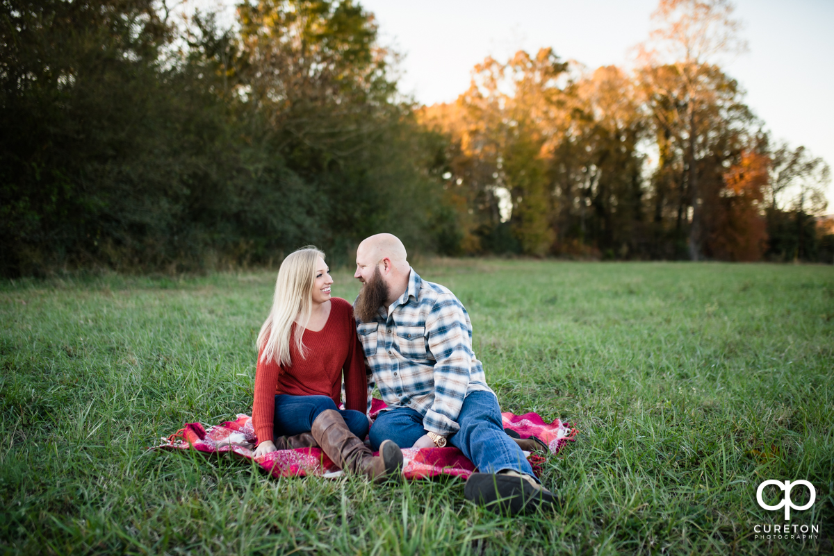 Engaged couple sitting on a blanket in a field.