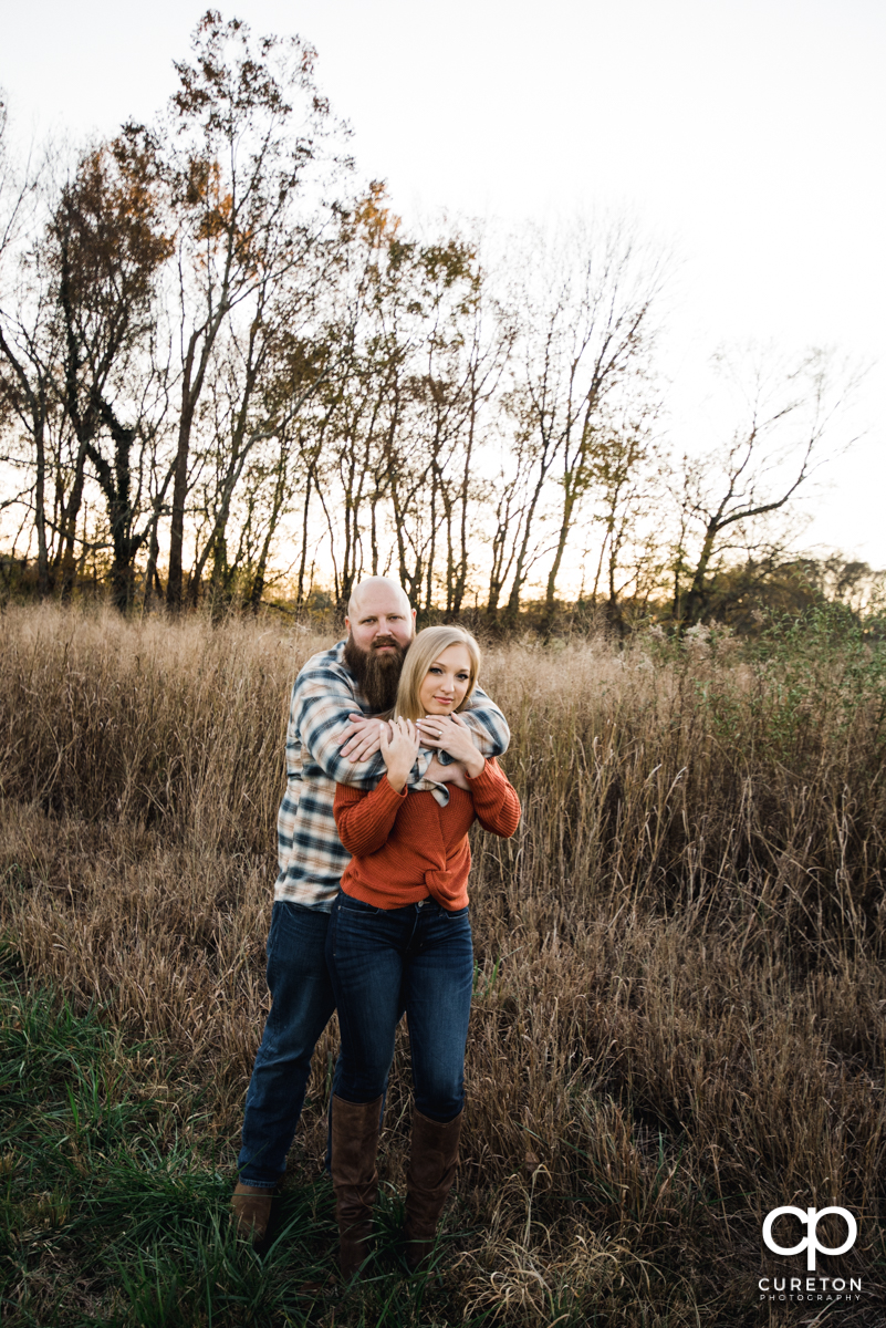 Man holding his fiancee in a field of tall grass.
