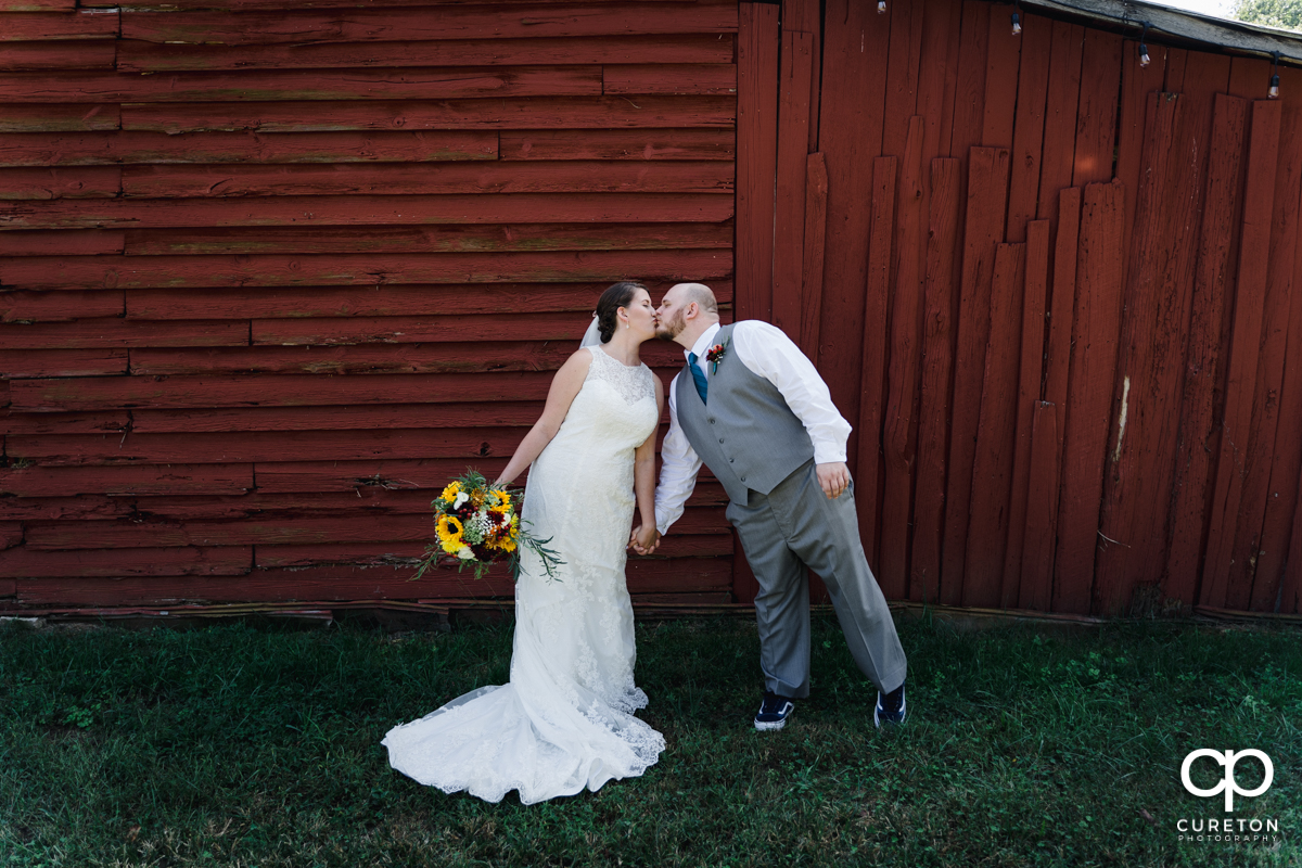 Bride and groom kissing in front of a red barn.