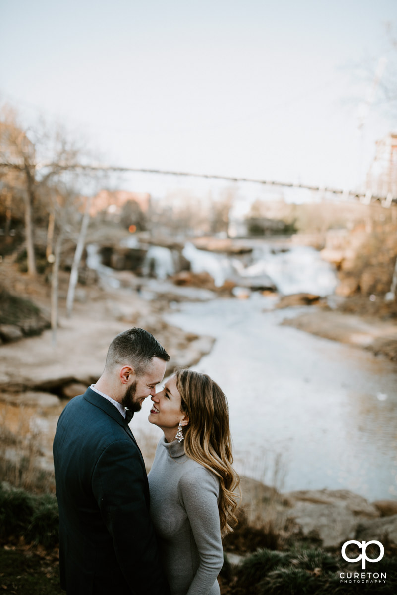 Bride and groom giving each other eskimo kisses with a bridge in the background.