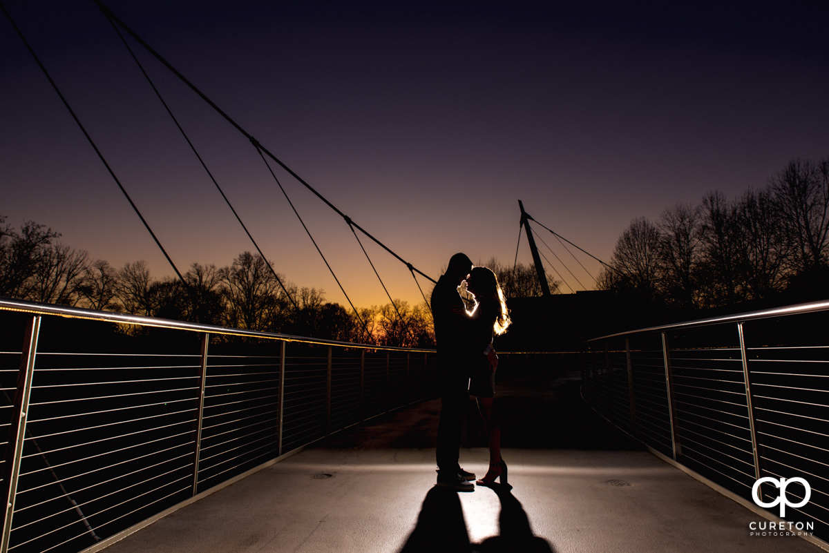 Future bride and groom hugging on the Liberty Bridge at sunset during a Falls Park Engagement session in downtown Greenville,SC.