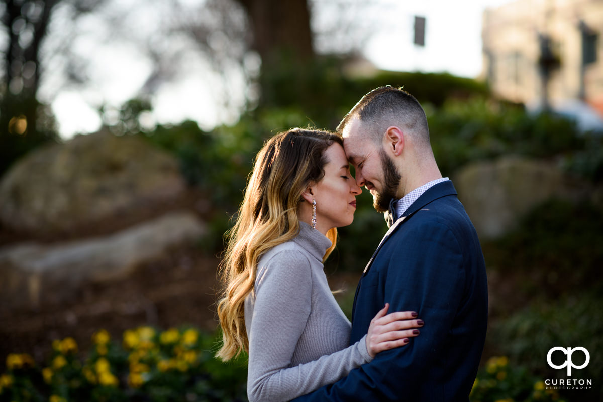 Engaged couple leaning on each other in the park.