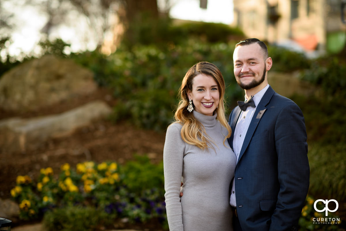 Man and woman standing in front of flowers during a downtown Greenville engagement session.