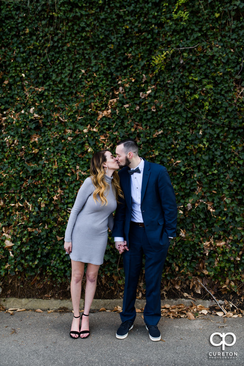 Man kissing his fiancee in front of a wall of ivy in Falls Park in Greenville.