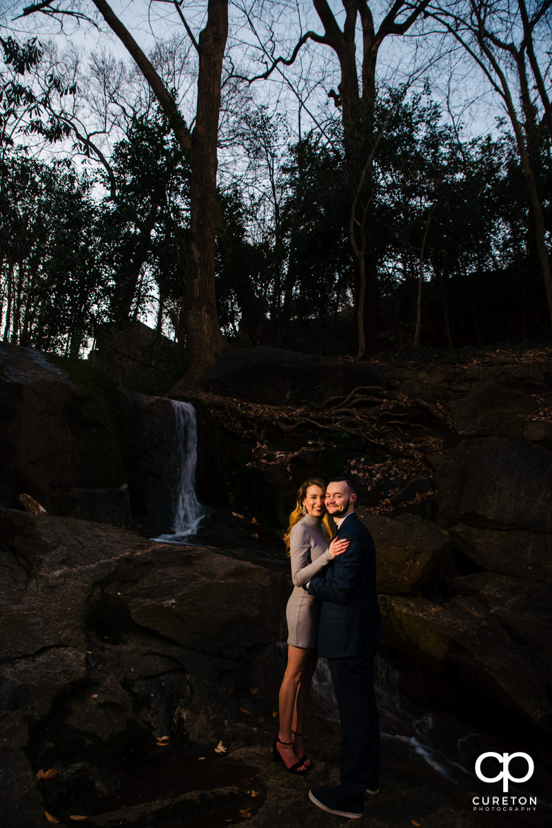 Engaged couple standing in front of a waterfall.