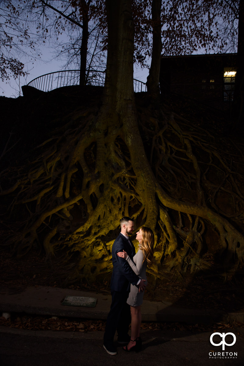 Future bride and groom standing in front of the landmark tree roots in Falls Park during an engagement session in downtown Greenville,SC.