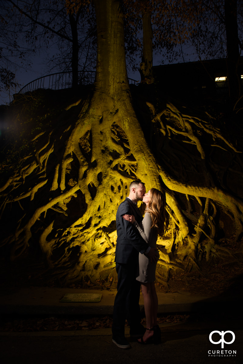 Future bride and groom kissing in front of the landmark tree roots in Falls Park during an engagement session in downtown Greenville,SC.