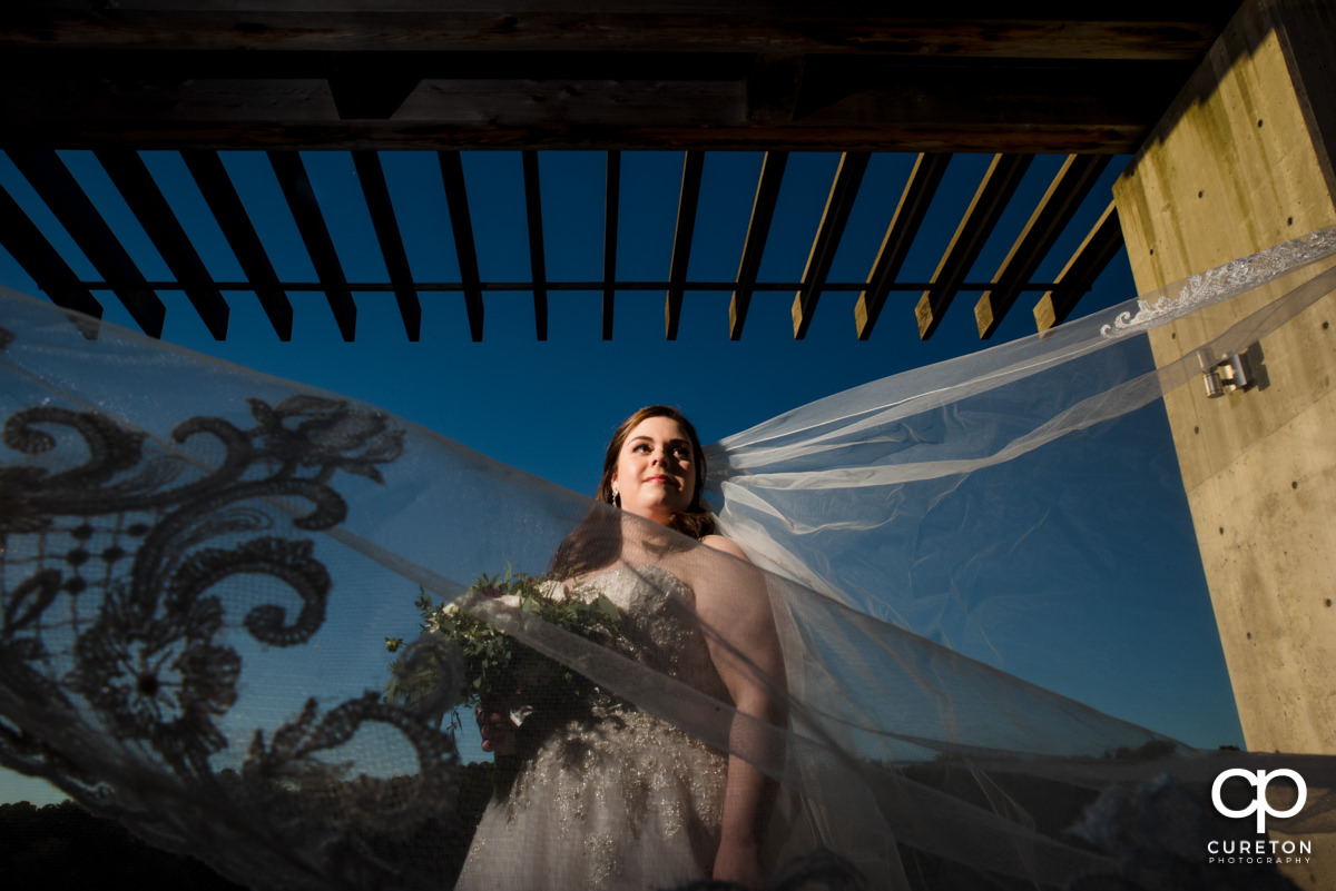 Bride underneath a portico by the lake at Furman University with her veil blowing in the wind.