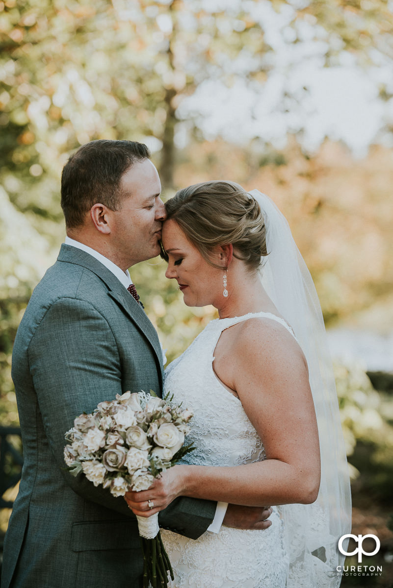 Groom kissing his bride on the forehead after their Furman rose garden wedding.