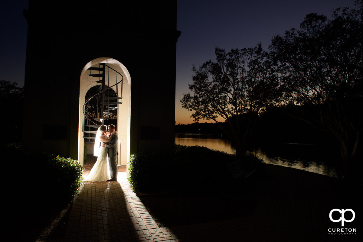 Backlit photo of a bride and groom at sunset in the bell tower at the Furman lake.