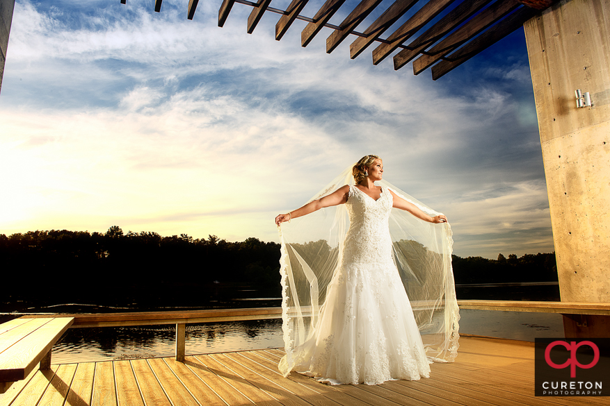 A bride with a long veil by the lake at sunset during her Furman University bridal session.
