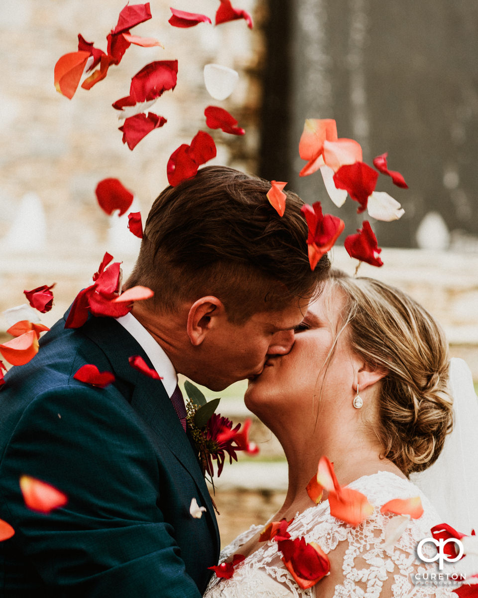 Bride and groom kissing as flower pedals fall around them on their wedding day in downtown Greenville,SC.