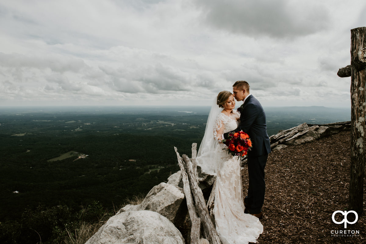 Bride and groom cuddling near a wooden cross behind Glassy Mountain on their wedding day.