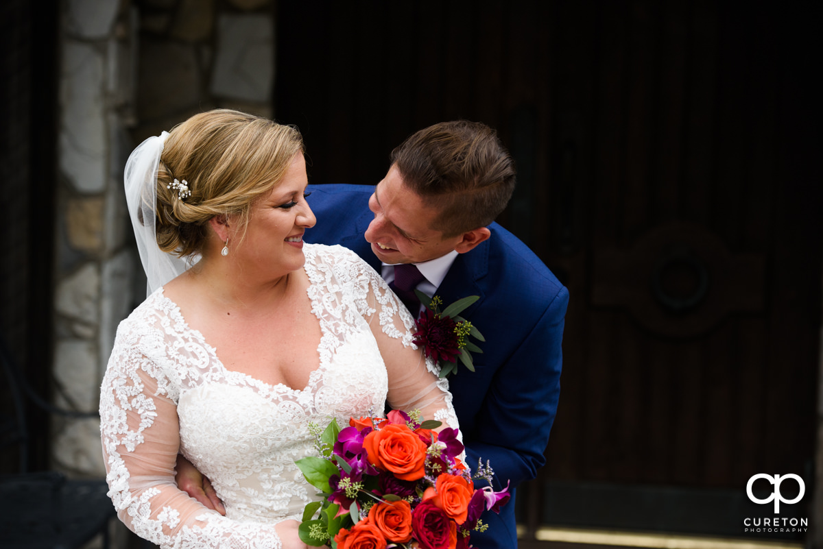 Bride and groom smiling at each other in front of the wedding chapel.