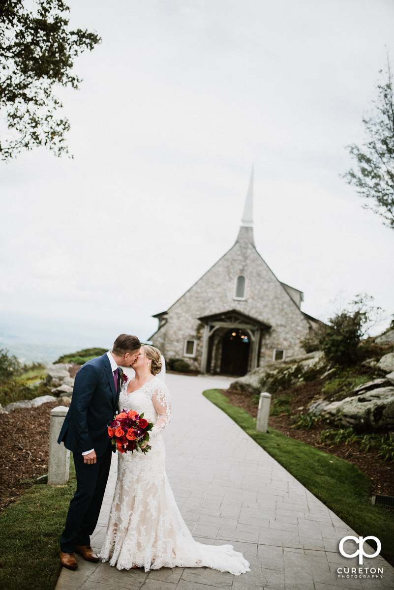 Bride and groom kissing with Glassy Chapel in the background.