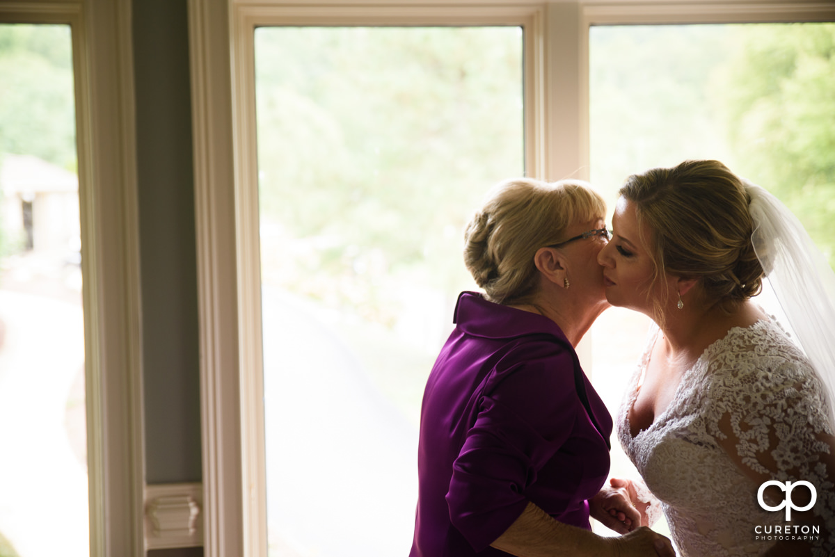Bride's mother kissing her on the cheek.