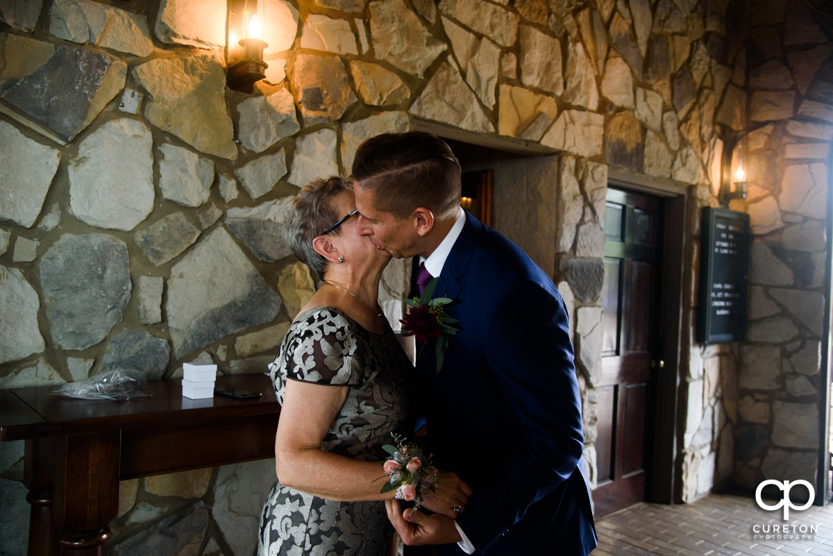 Groom kissing his mom on the cheek.