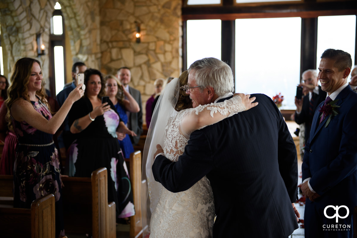 Bride hugging her dad as he gives her away at the wedding ceremony.