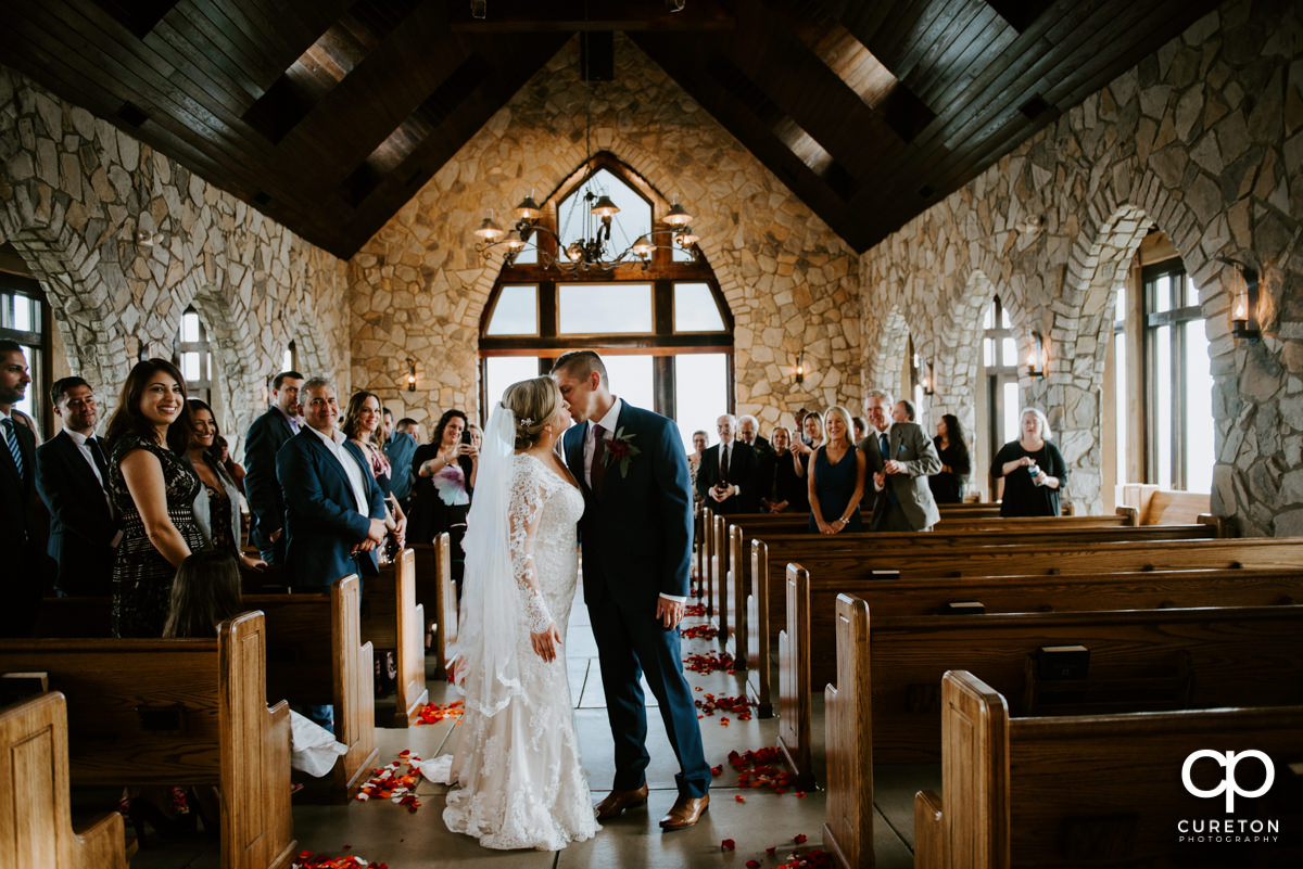 Bride and groom stopping for a kiss as they exit the wedding ceremony at Glassy Chapel.