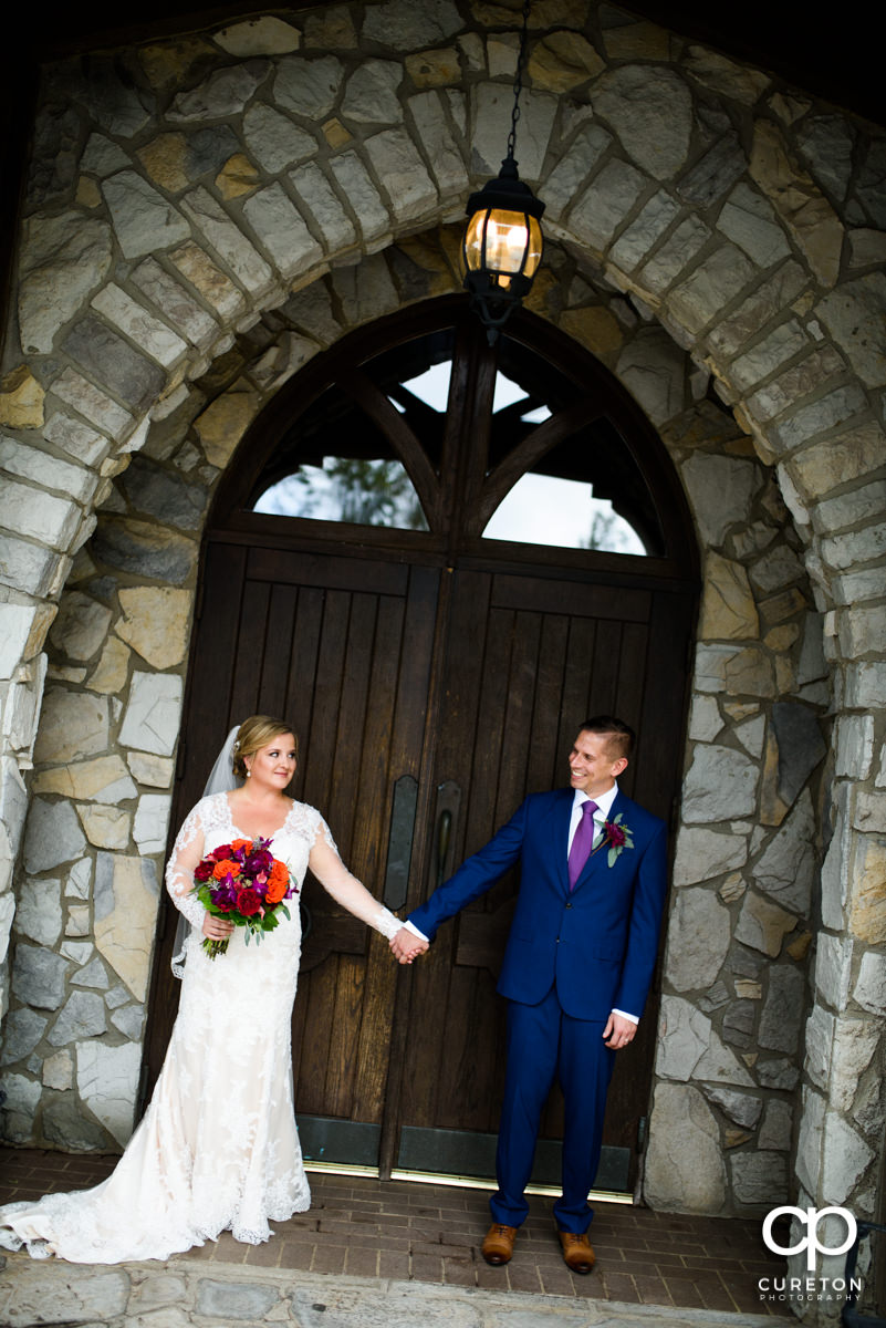 Bride and groom holding hands in front of the doors at Glassy Chapel.