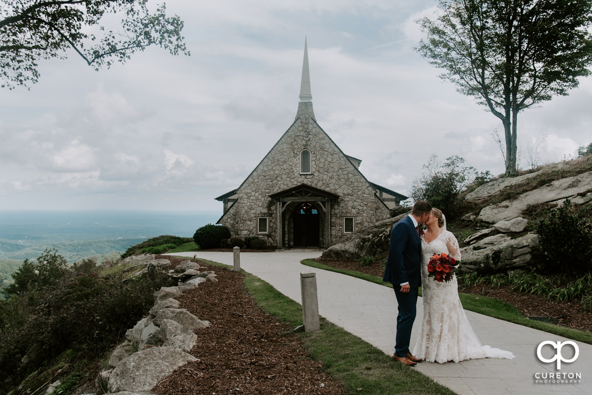 Bride and groom kissing in front of Glassy Chapel after their wedding ceremony in Landrum,SC.