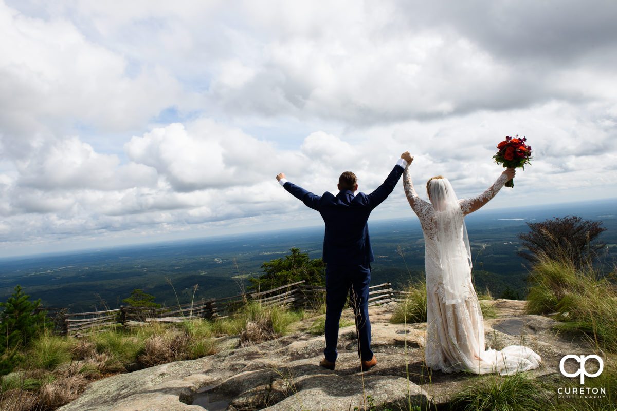 Groom and bride holding their hands in the air on the top of Glassy Chapel.