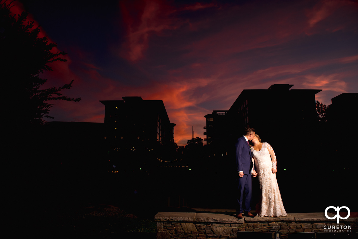Bride and groom kissing at sunset in front of the downtown Greenville,SC skyline outside of their Larkin's Cabaret Room wedding reception.