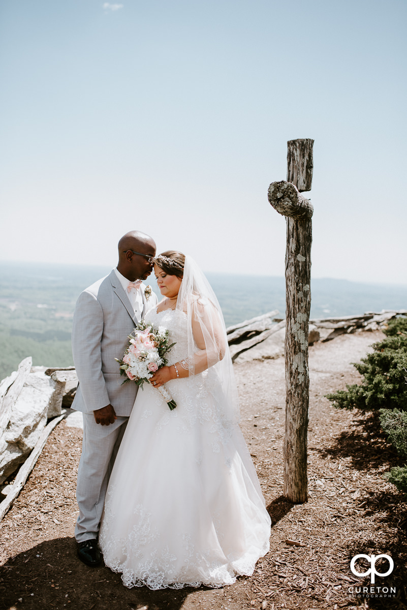 Bride and groom standing near a wooden cross on a mountain top after their wedding ceremony at the Cliffs Glassy Chapel.