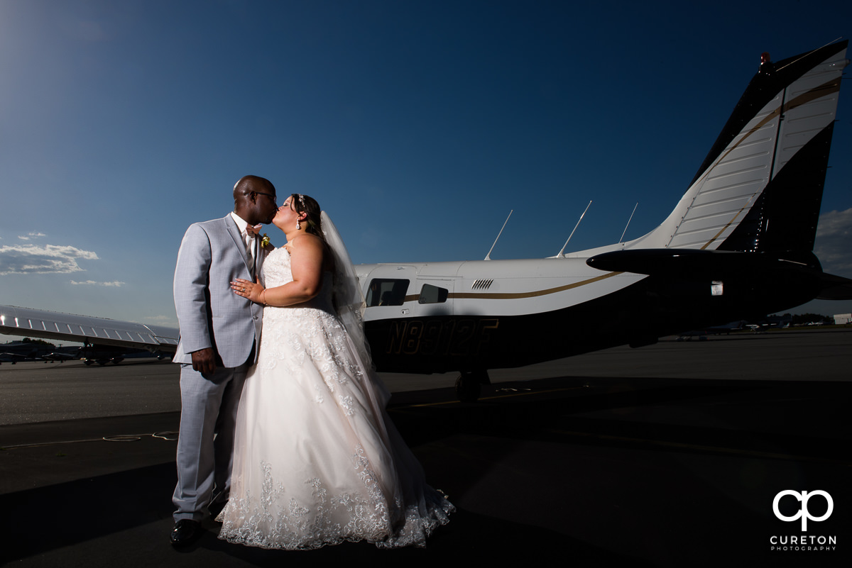 Bride and groom kissing beside an airplane at their wedding reception at the Runway Cafe Hangar in Greenville,SC.