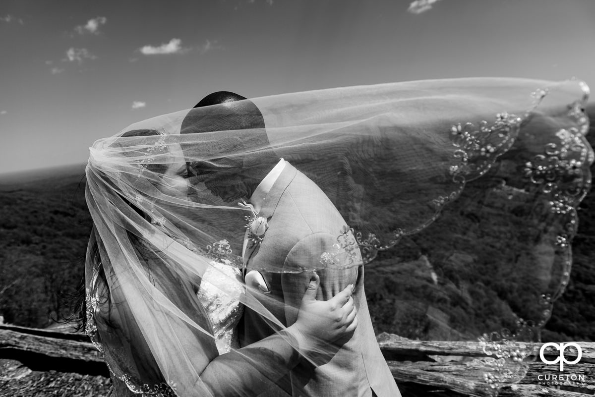 Bride and groom snuggling at Glassy Chapel with her veil blowing in the wind over their faces after their wedding.
