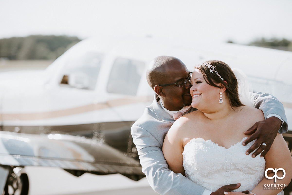 Groom hugging his bride beside an airplane.