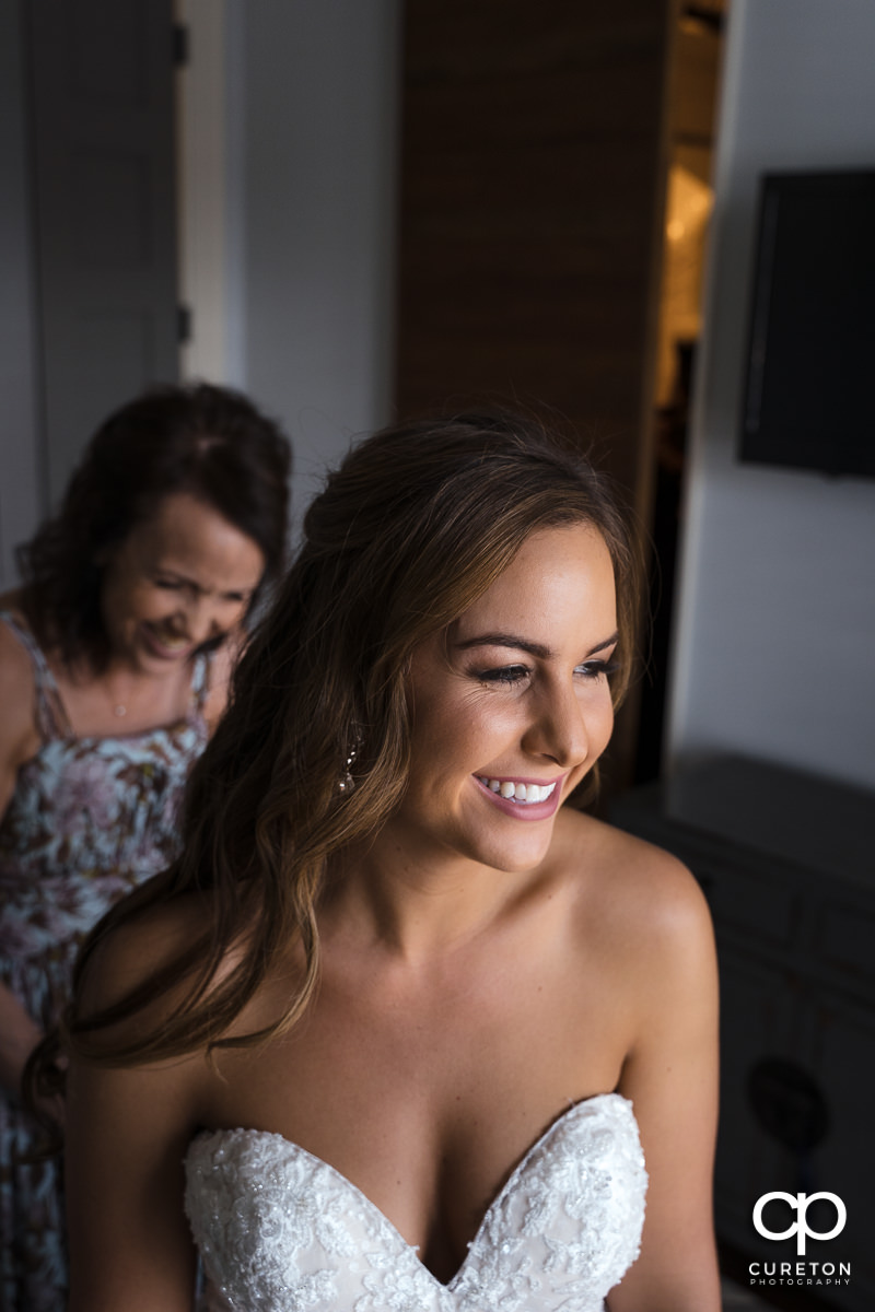 Bride smiling as her mother helped her into her wedding dress.