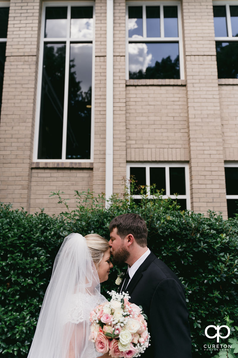 Groom kissing his bride on the forehead.