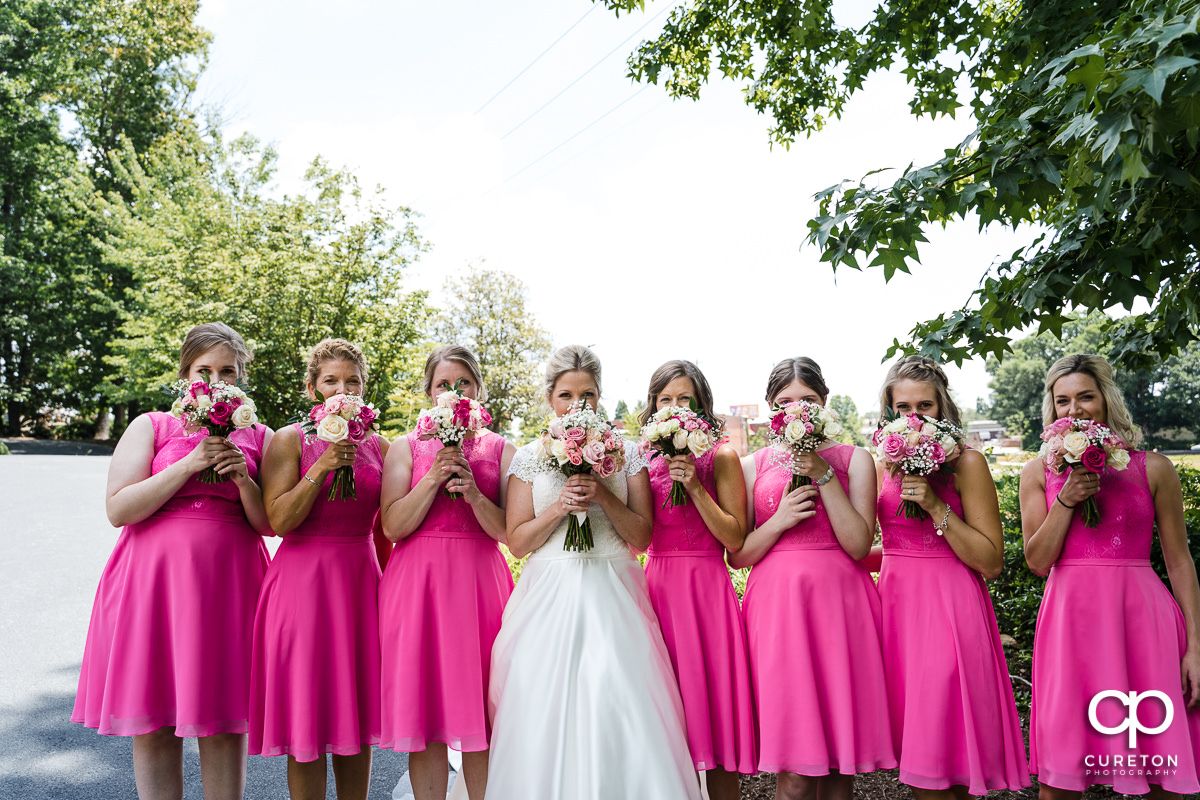 Bride and bridesmaids holding flowers over their faces.