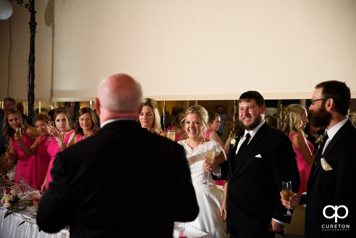 Bride and groom listening to her father give a speech.