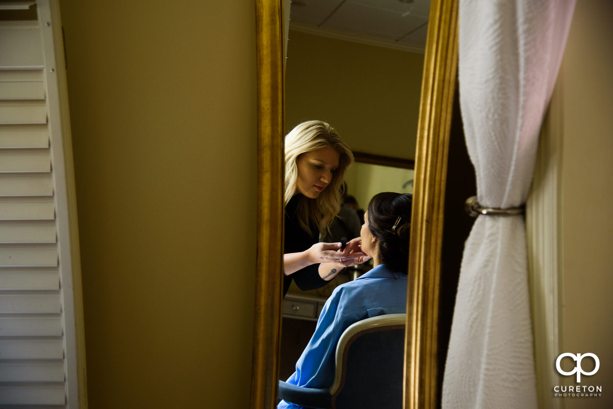 Bride getting makeup applied in the mirror.