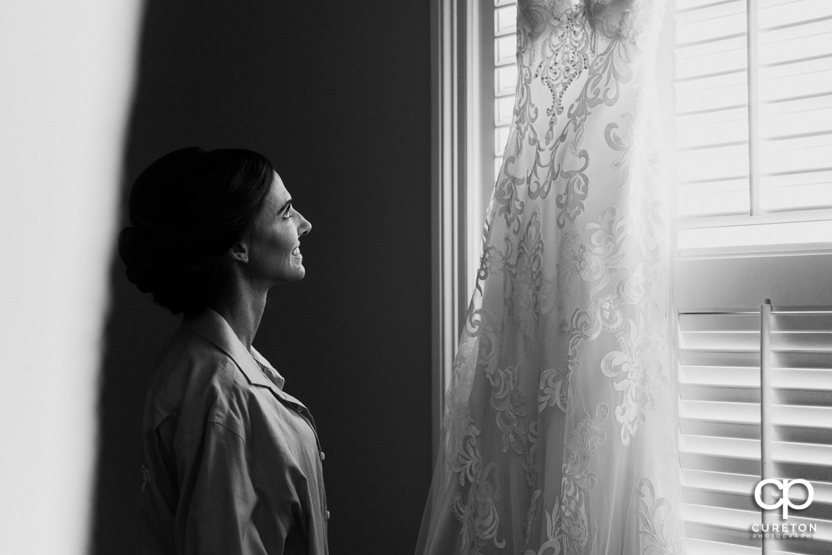 Bride looking at her dress hanging in the window.