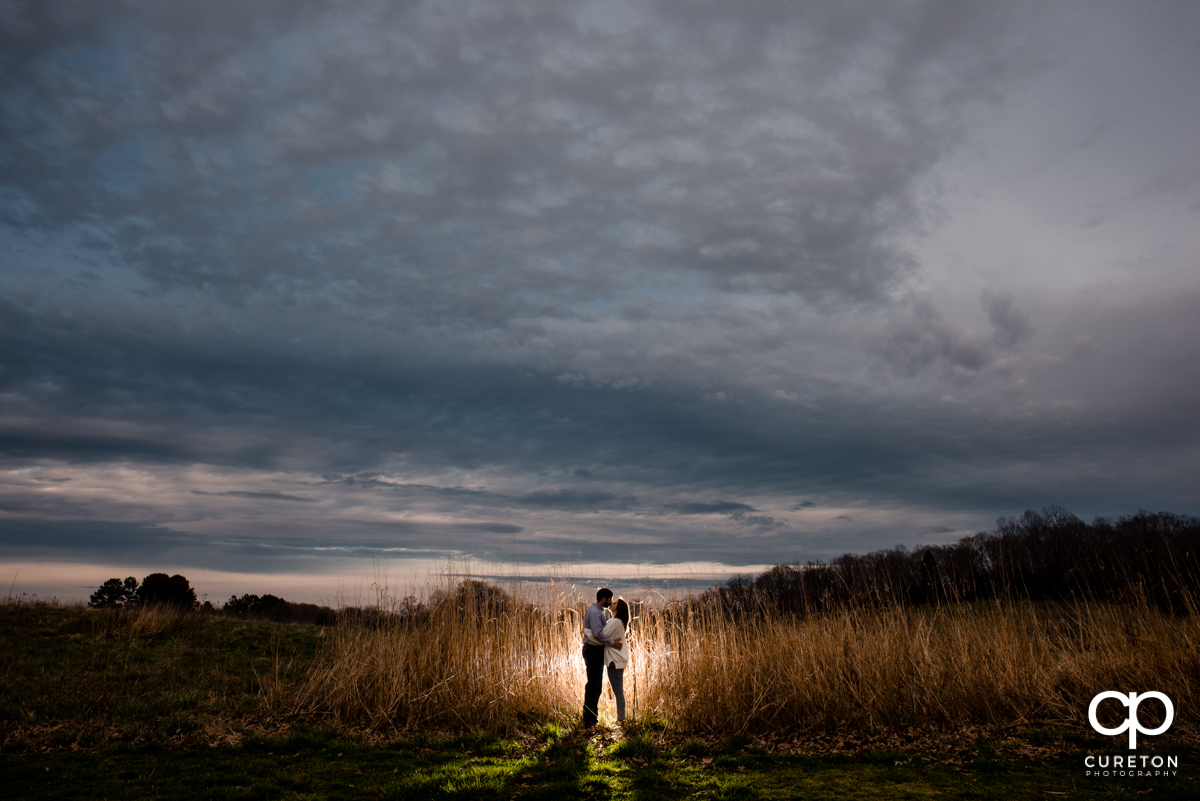 Man and his bride standing in some tall grass at sunset during a Greenbrier Farms engagement session.